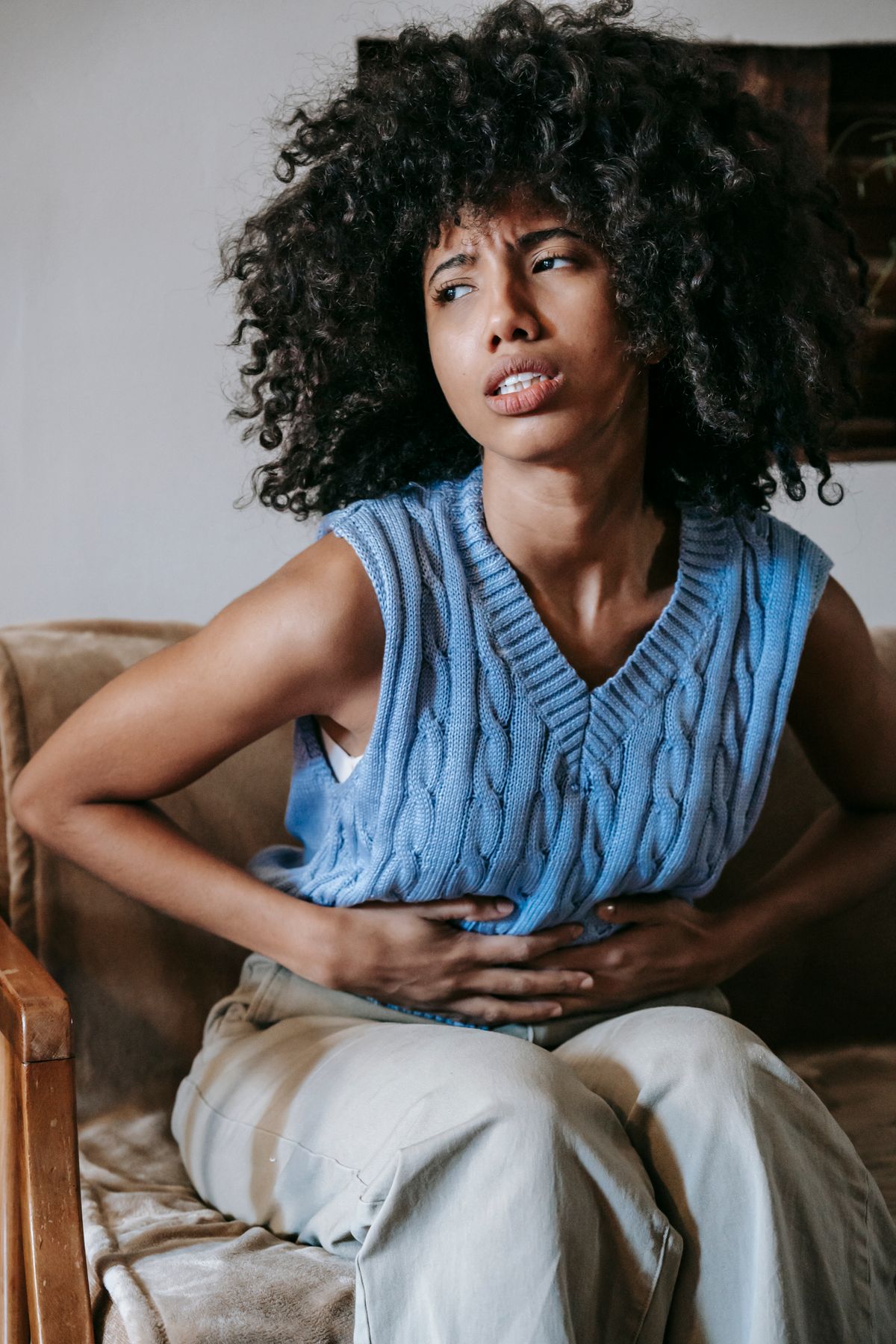 Black African woman sitting on couch holding her lower abdomen in menstrual pain – women's health Nigeria