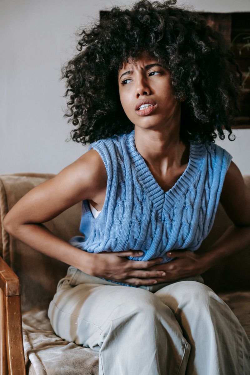 Black African woman sitting on couch holding her lower abdomen in menstrual pain – women's health Nigeria
