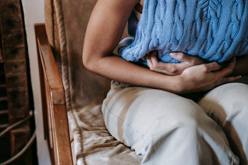 Free Crop unrecognizable female touching belly while having acute pain in stomach sitting on couch Stock Photo