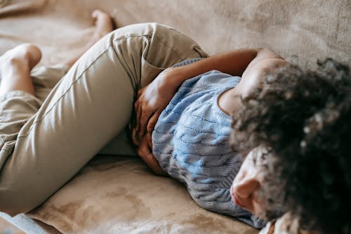 Free From above of crop anonymous African American female lying on couch and touching belly while having stomach ache Stock Photo