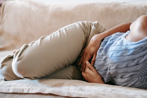 Free Crop faceless female in casual wear lying on sofa while having acute pain in stomach Stock Photo