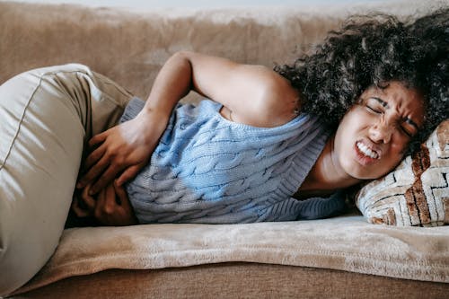 Free Woman Suffering from a Stomach Pain Lying Down on Couch Stock Photo