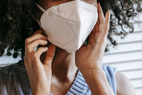 Closeup of crop anonymous African American female wearing white protective mask on face