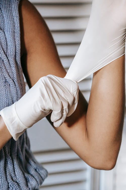 Crop faceless female in sleeveless sweater wearing white medical rubber gloves to protect hands
