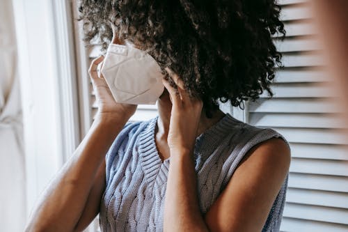 Side view of anonymous African American female in casual clothes wearing white protective face mask