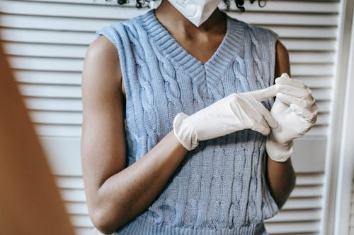 Crop anonymous African American female in casual outfit and wearing white protective face mask and medical rubber gloves
