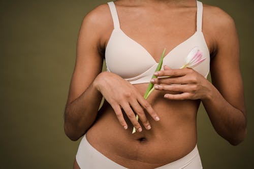Free Crop unrecognizable African American female in white lingerie with hairs on arms standing against beige background with tulip in hands Stock Photo