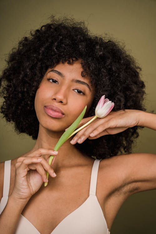 Alluring young ethnic female holding tulip near face and looking at camera