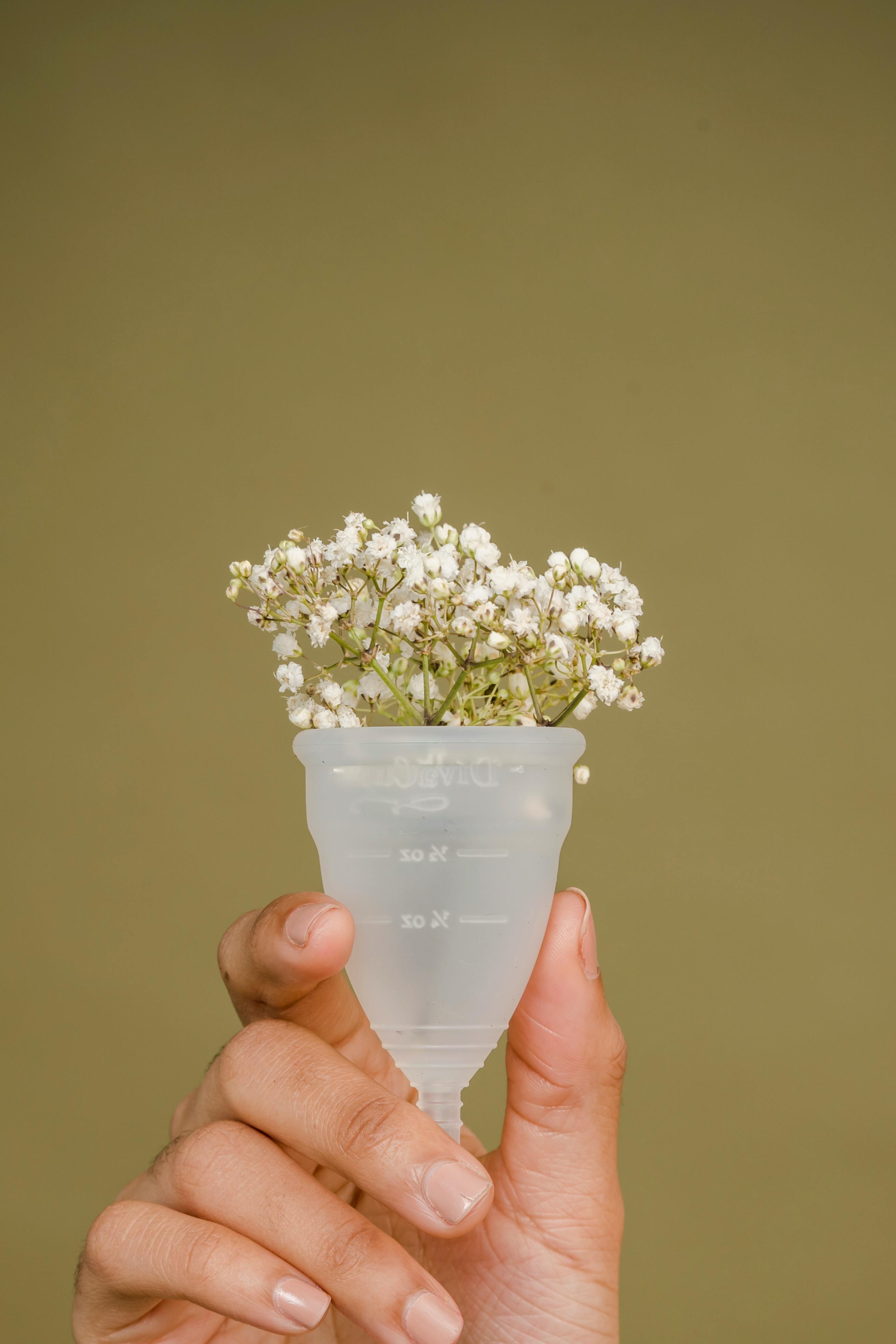 crop woman holding menstrual cup in hand with tiny white flowers