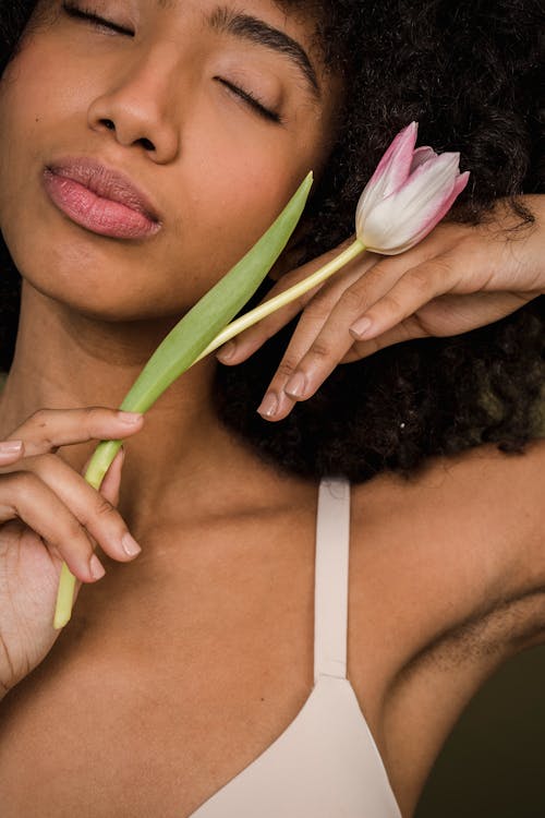 Calm young ethnic lady touching flower gently with closed eyes