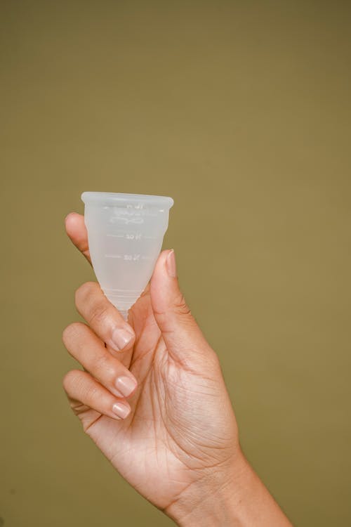 Free Crop faceless woman demonstrating small white silicone menstrual cup in hand against beige background Stock Photo