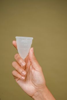 在米色背景下，一位无脸妇女手持白色小硅胶月经杯进行展示