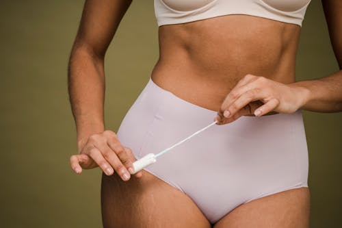 Crop anonymous female in bra and panties showing female tampon on olive background