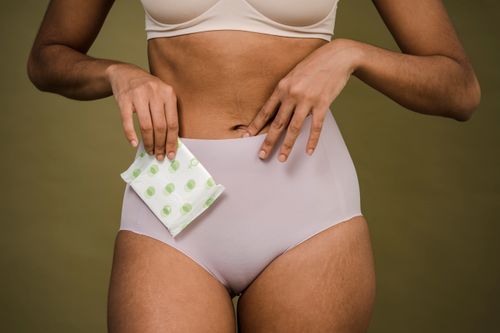 Free Crop anonymous female in pink bra and panties with sanitary pad for critical period on olive background Stock Photo