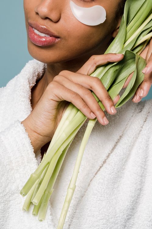Free Crop anonymous African American female with eye patches showing green tulip stems on blue background Stock Photo