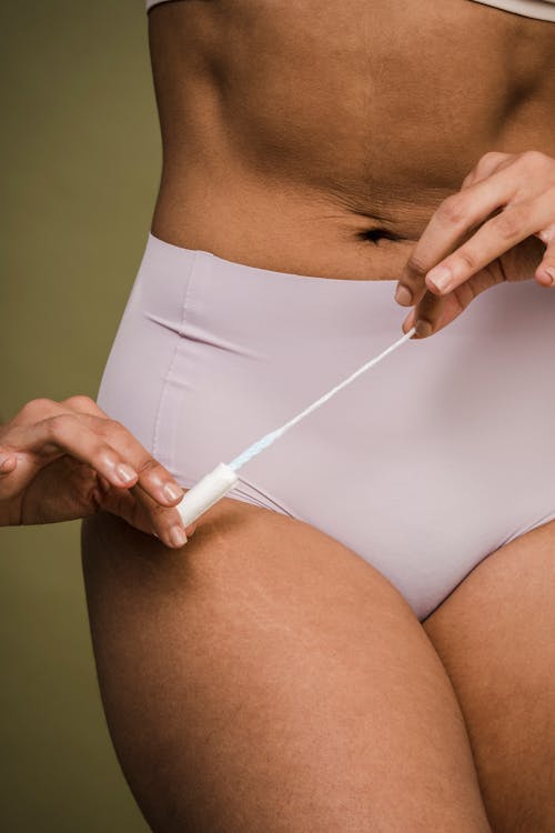 Ethnic woman in underwear holding feminine tampon