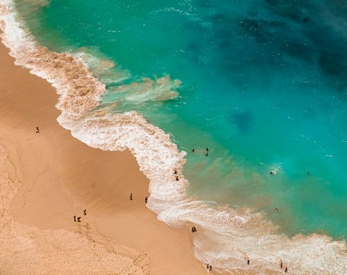 Free A stunning aerial view of a beach with turquoise waves crashing gently on the sandy shore, people enjoying the water. Stock Photo