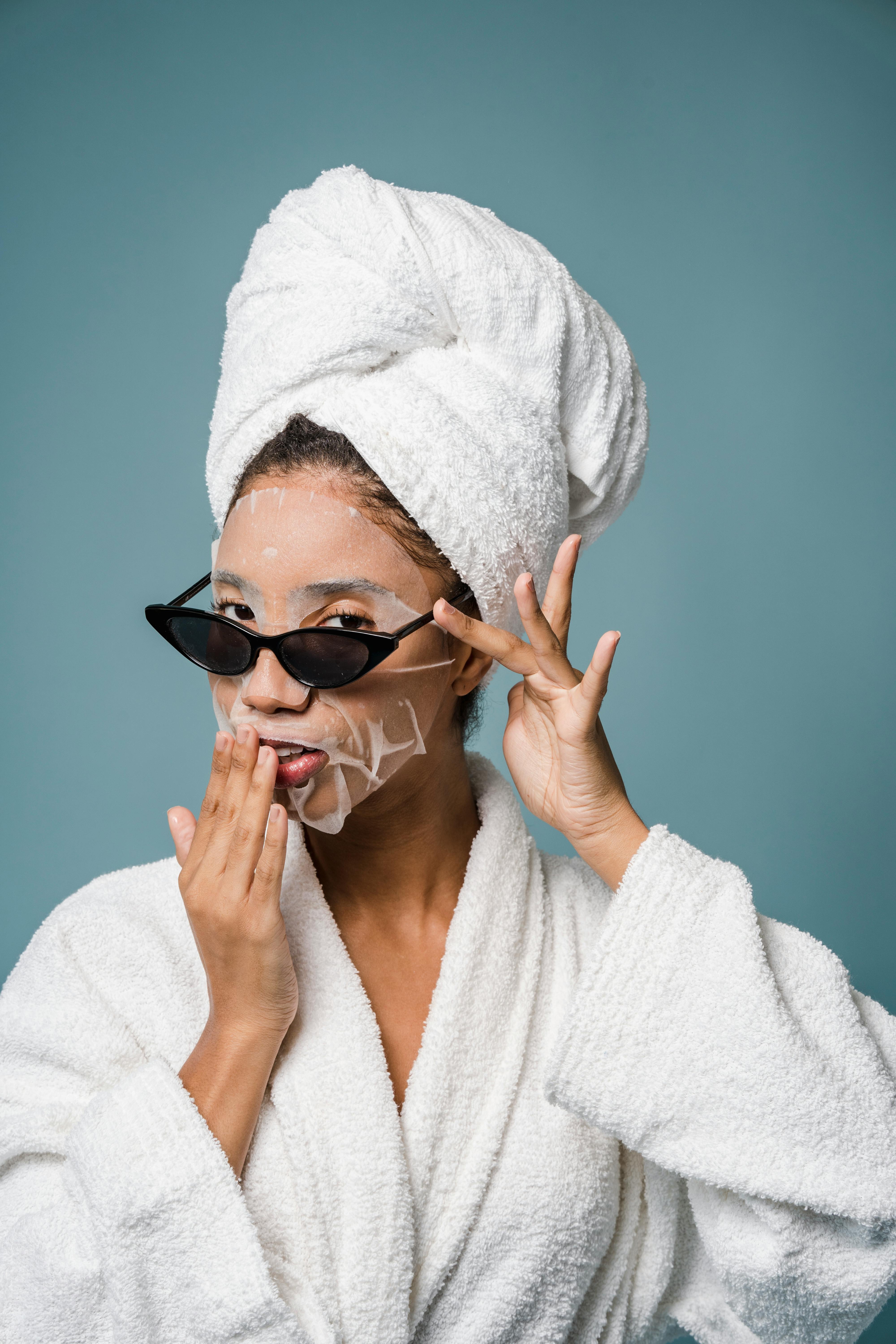 charming black female with moisturizing sheet mask in bathrobe in studio