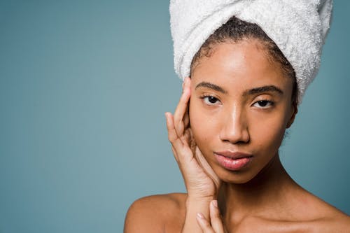 Black woman in white towel turban touching face and looking at camera