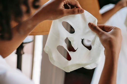 Ethnic female holding sheet mask at home