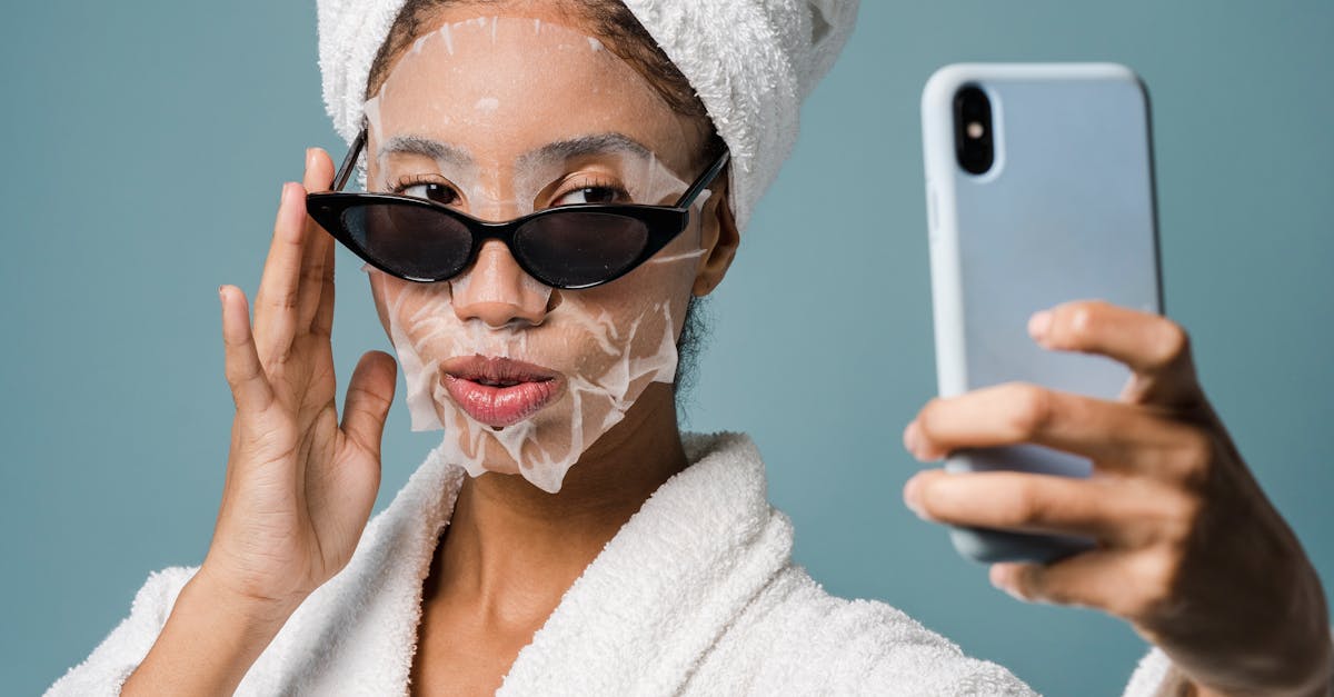 Confident black female with sheet mask taking selfie on smartphone