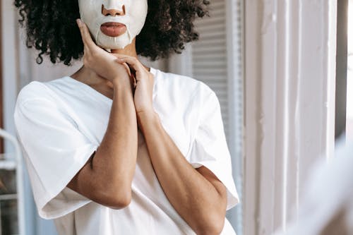 Ethnic female in sheet mask looking at mirror