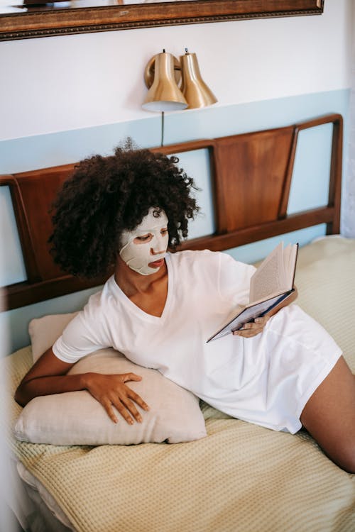 African American female in sheet mask reading book in bedroom