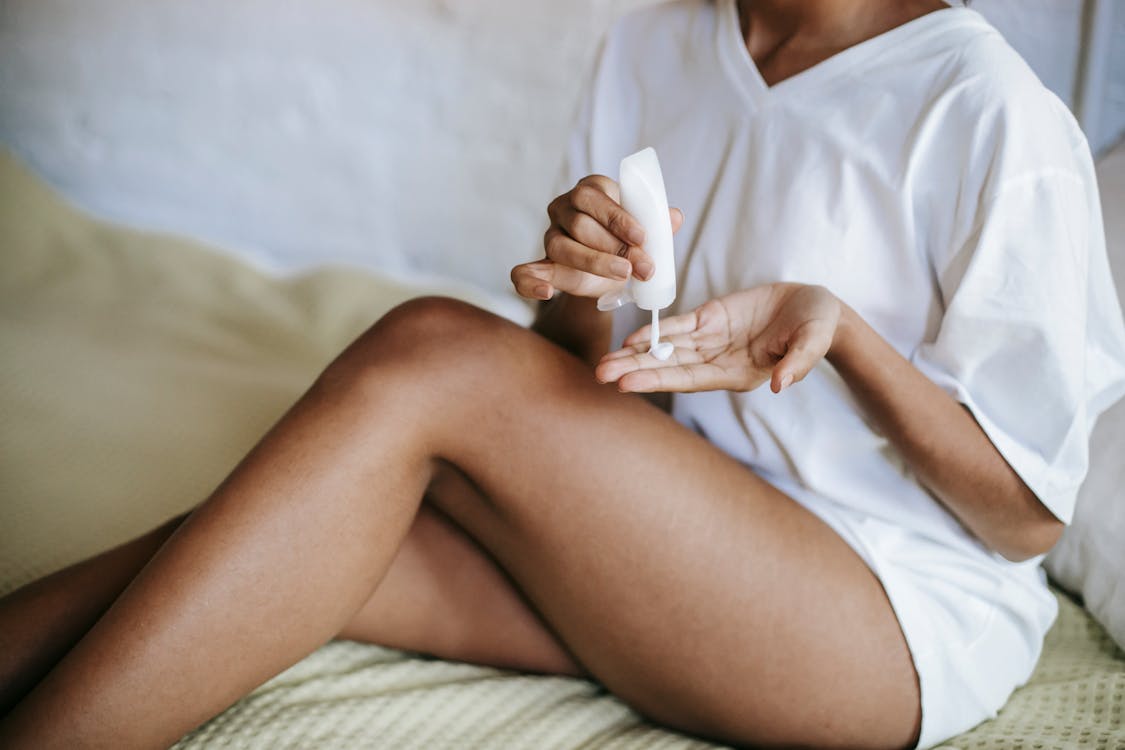 Woman with cosmetic product sitting on bed