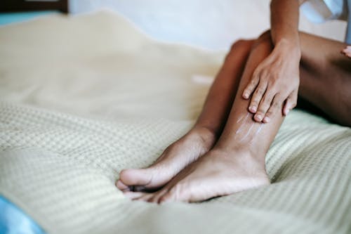 Free Crop woman moisturizing legs on bed Stock Photo