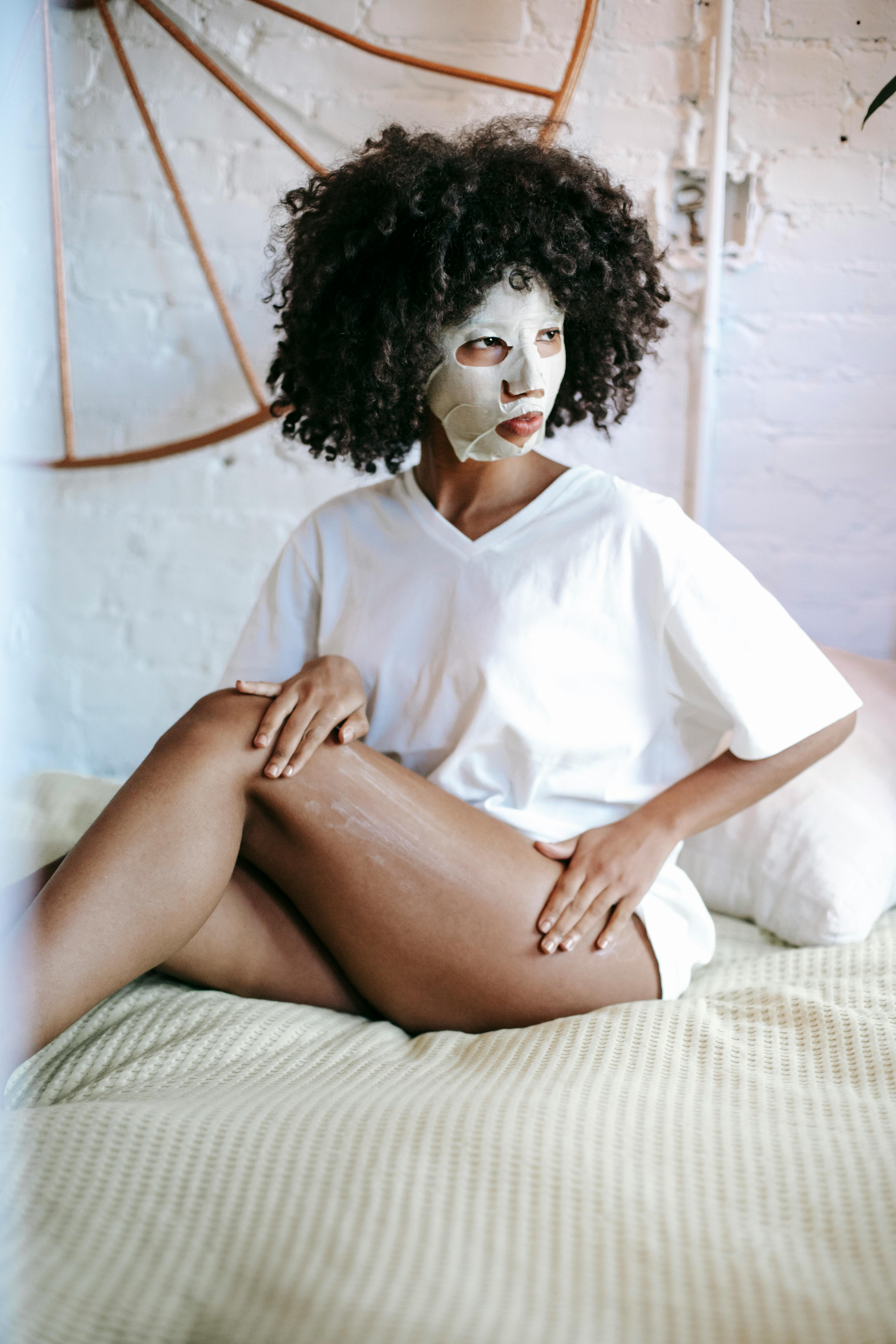 black woman with facial mask on bed