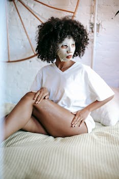 A young woman applies skincare products while relaxing at home, wearing a face mask.
