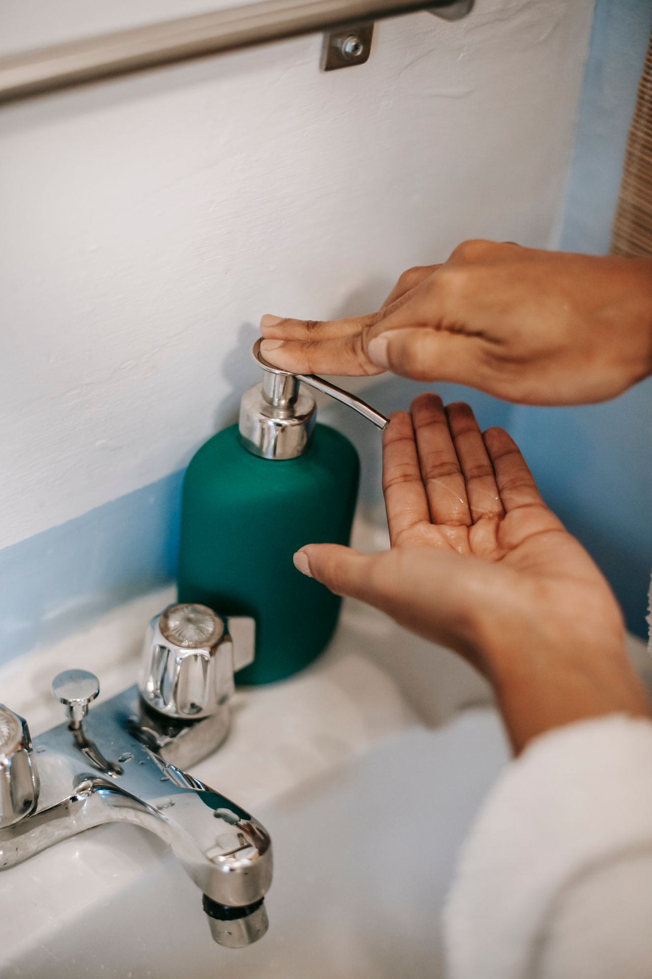 Hand pressing a green pump soap dispenser at a bathroom sink