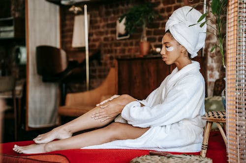 Woman in bathrobe applying cream on leg