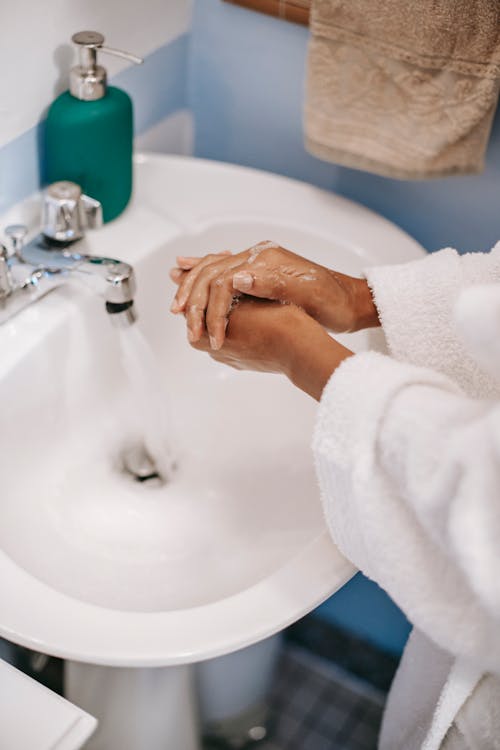 白いセラミックシンクで手を洗う白いバスローブの人