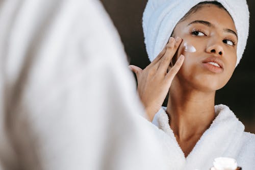Free Ethnic woman applying cream on face in morning Stock Photo