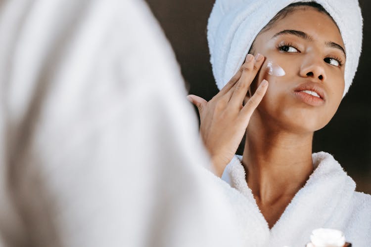 Ethnic Woman Applying Cream On Face In Morning