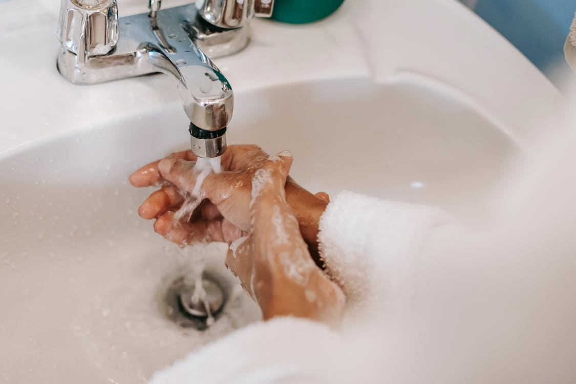 Free High angle of crop anonymous ethnic female washing hands with foamy water during morning hygiene routine Stock Photo