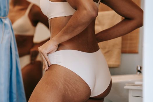 Crop anonymous ethnic woman adjusting panties on butt with stretch marks in bathroom