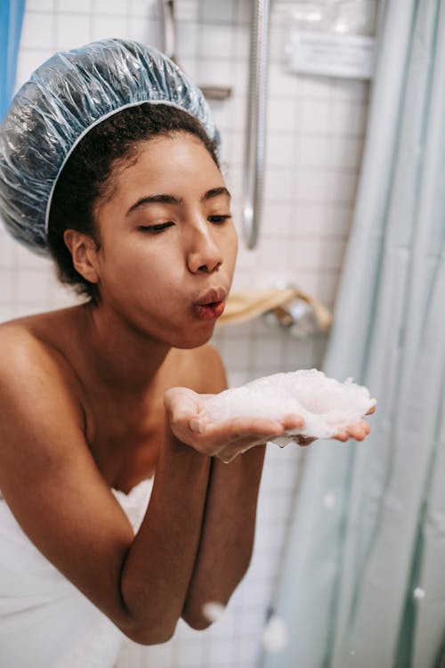 Ethnic woman blowing foam from hands in bathroom