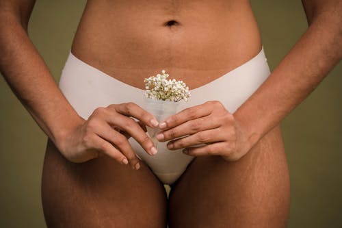 Free Crop unrecognizable female with stretch marks on hips in white underwear holding menstrual cup with delicate flowers in hands against green background Stock Photo