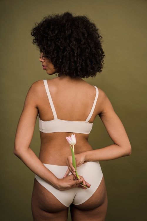 Free Back view of unrecognizable young African American female with curly hair in white  lingerie standing in green studio with delicate tulip flower in hands Stock Photo