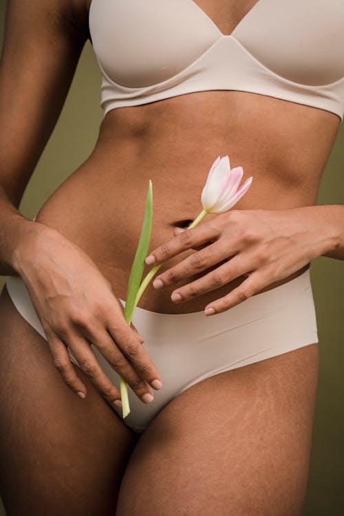 Unrecognizable woman in lingerie standing in green studio with flower in hands