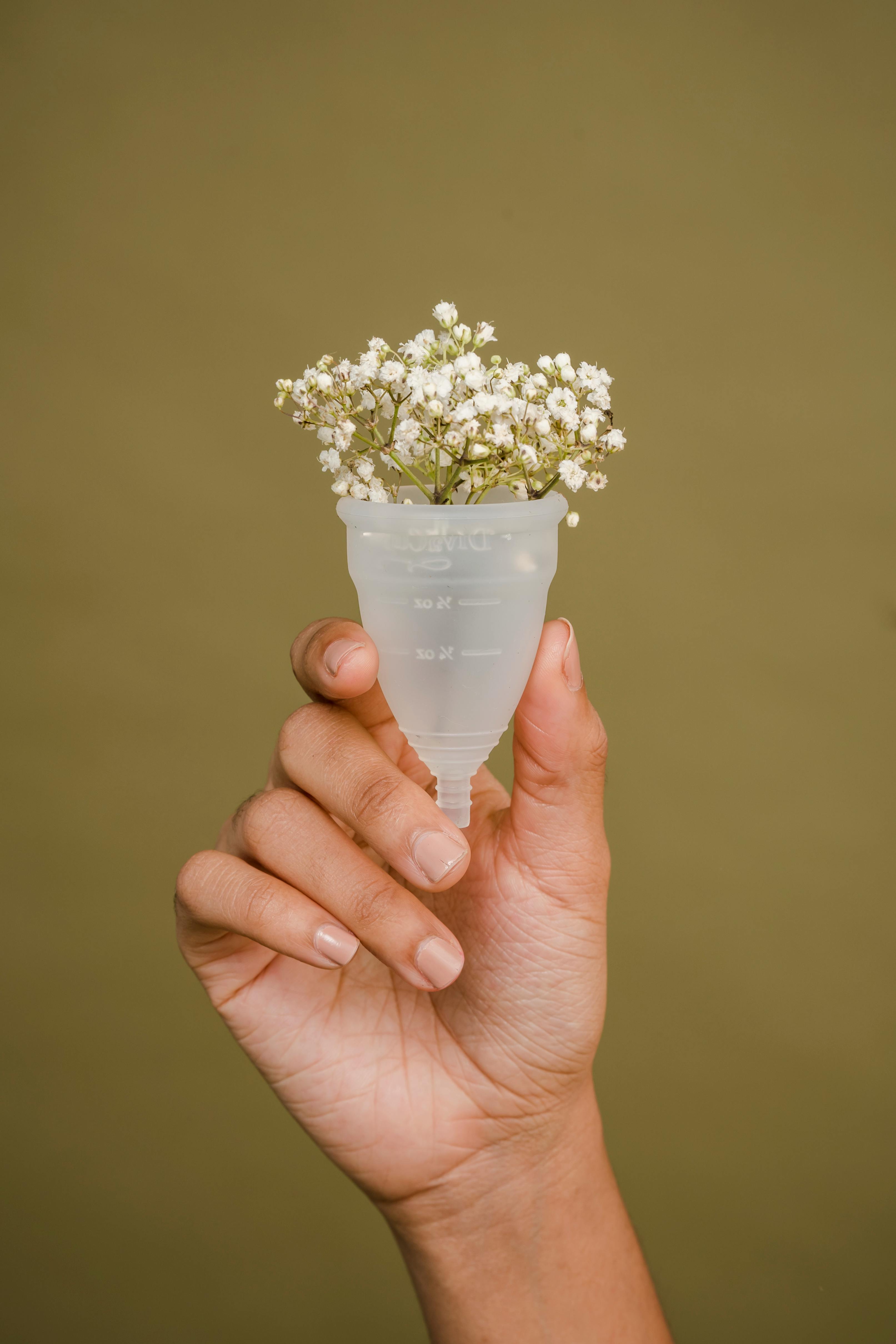 faceless woman showing menstrual cup with tender white flowers