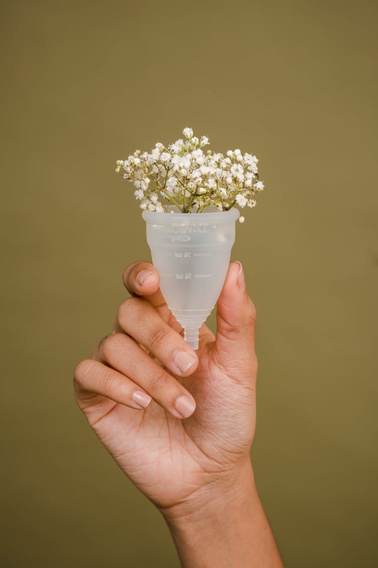 Faceless Woman Showing Menstrual Cup With Tender White Flowers