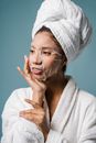 Smiling young ethnic female applying sheet mask on face after shower