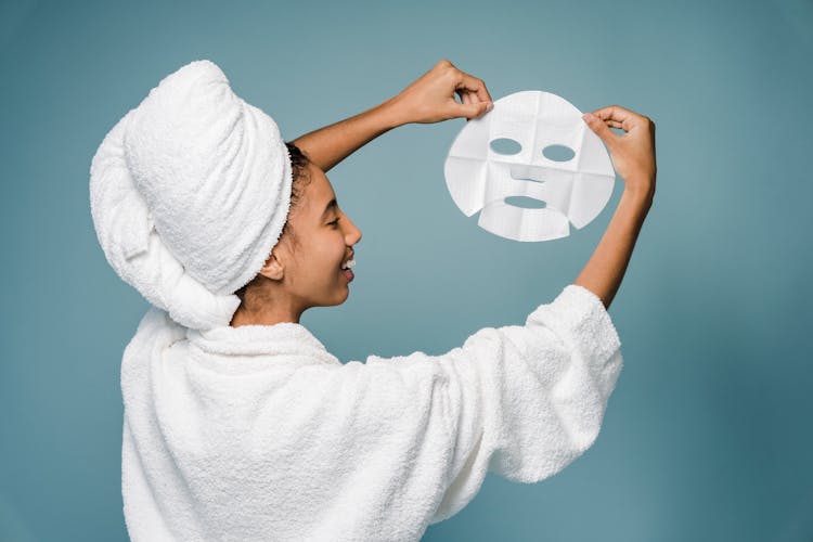 Cheerful Young Black Lady Showing Sheet Mask And Smiling After Bath