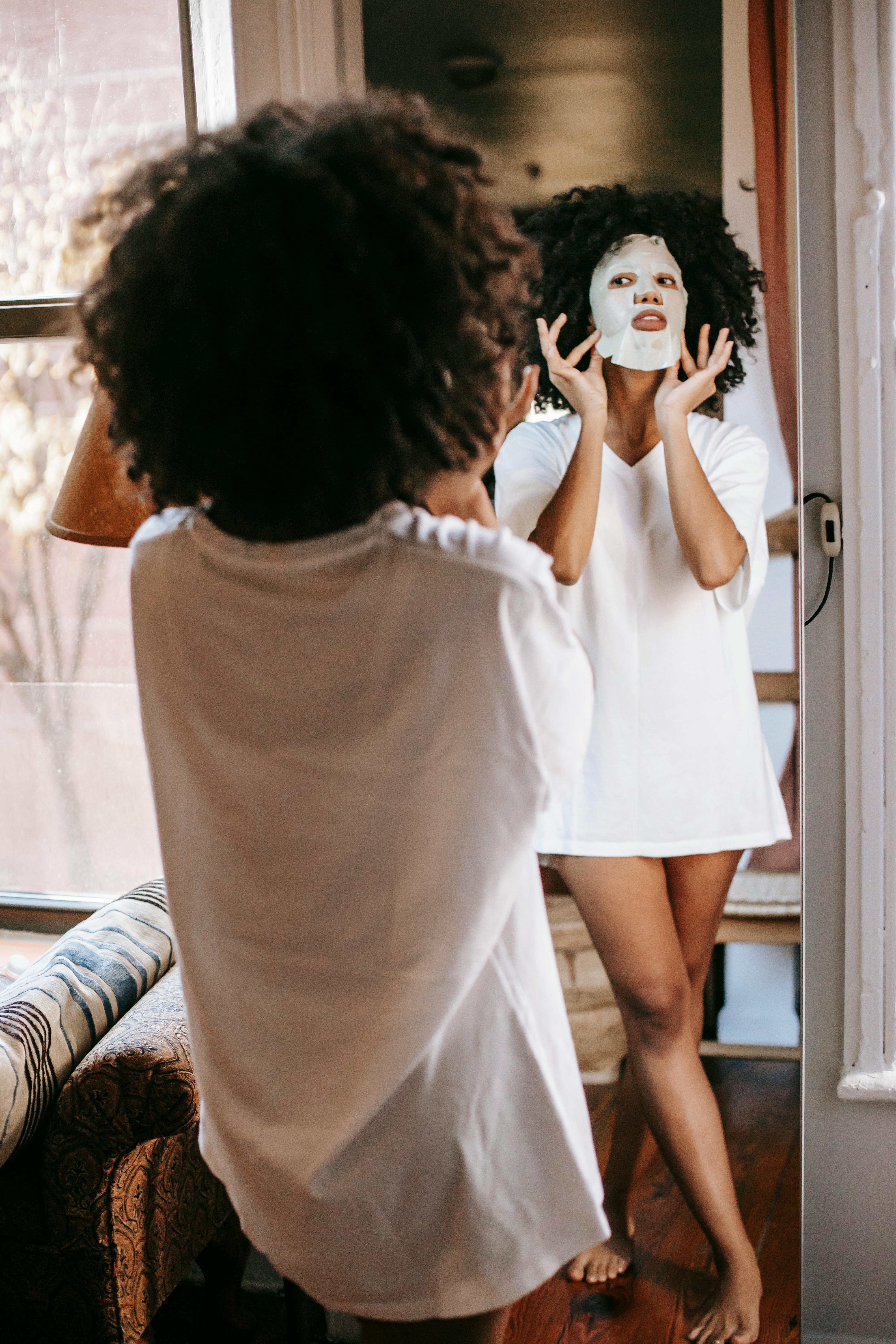african american woman with sheet mask looking in mirror