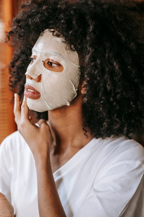 Free Confident young black female touching face covered with sheet mask Stock Photo