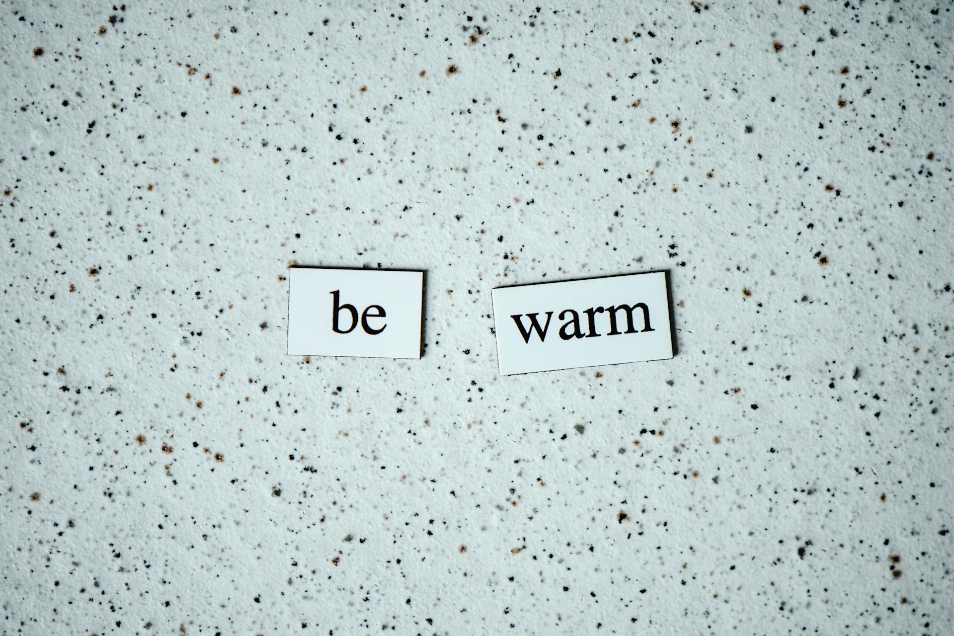 Close-up shot of 'be warm' text on a speckled surface, conveying warmth and positivity.