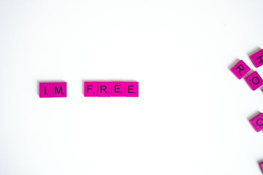 Pink scrabble tiles with the text 'I'M FREE' on a white surface, offering a symbolic message of freedom.